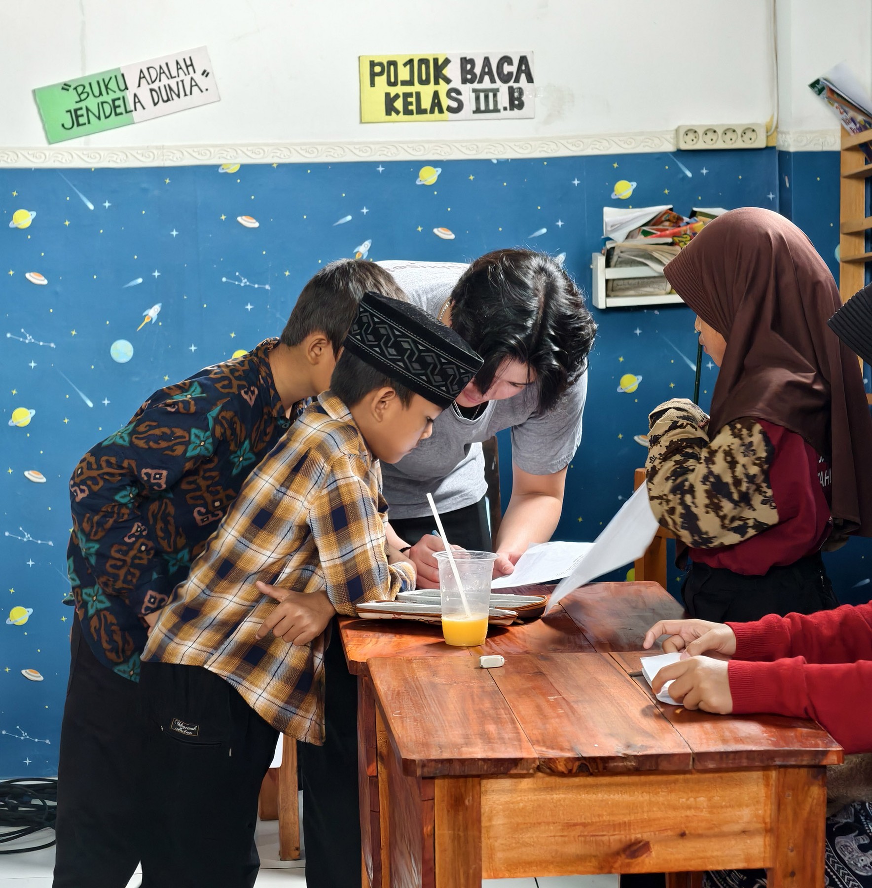 An Abhipraya volunteer helping students with a writing activity at their classroom desk