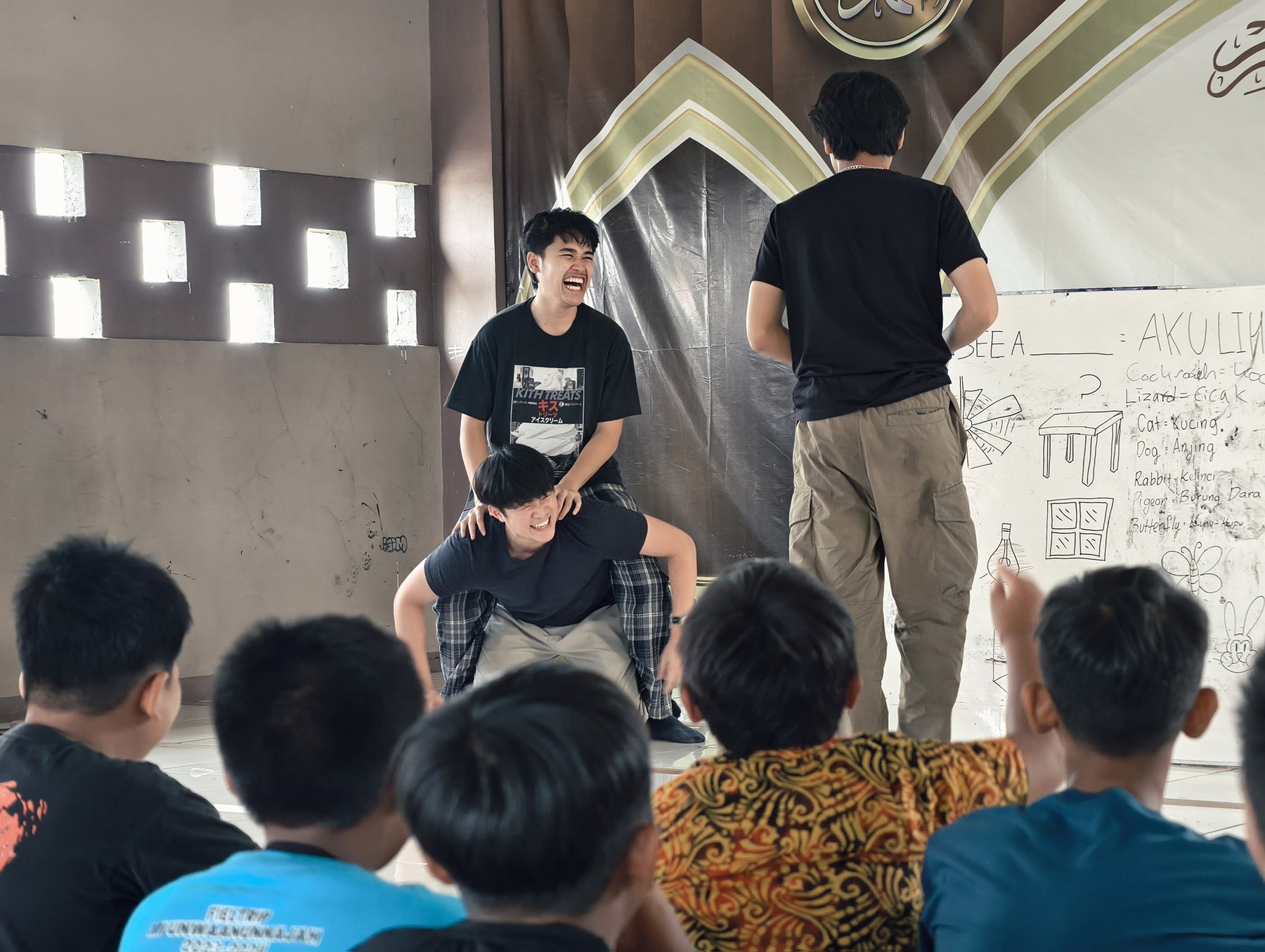 Two Abhipraya volunteers leading a lesson in front of a whiteboard and a seated group of students
