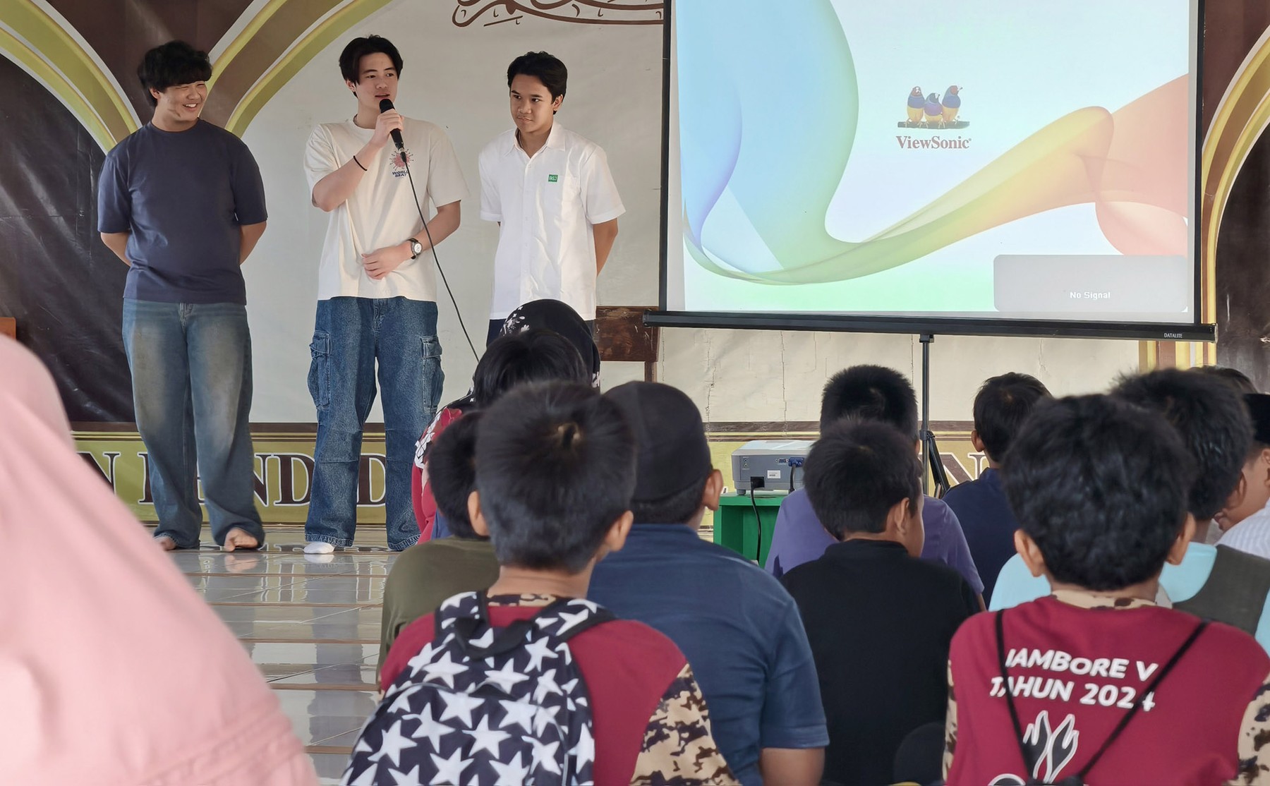Abhipraya volunteers speaking to students beside a projected classroom presentation