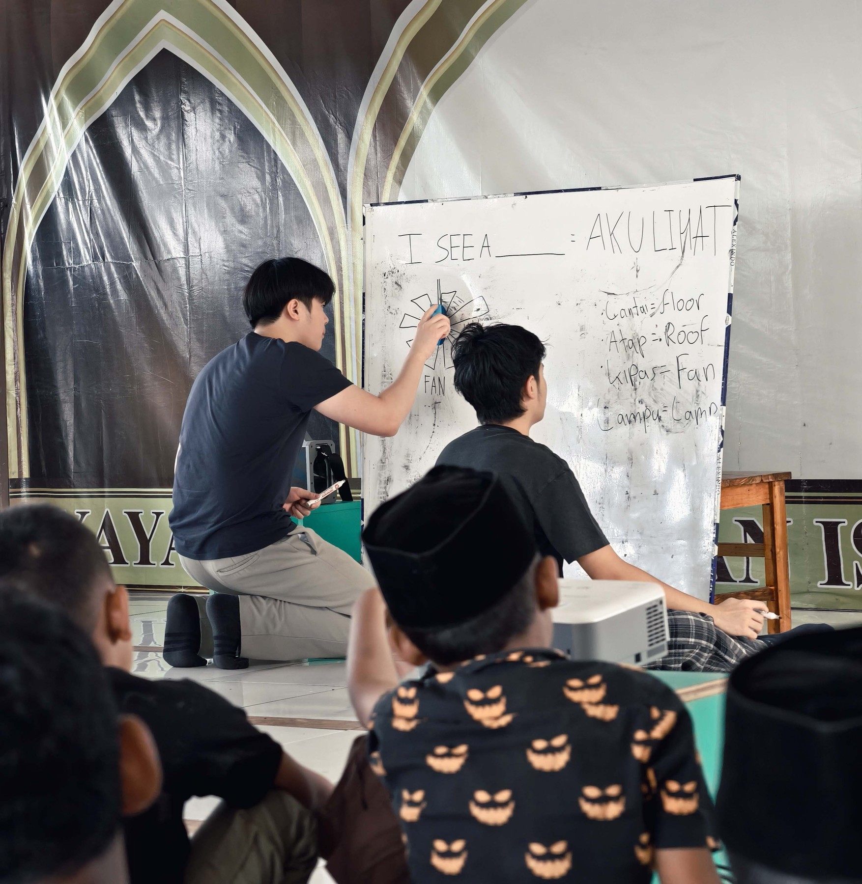 An Abhipraya volunteer explaining a lesson at the whiteboard as students watch