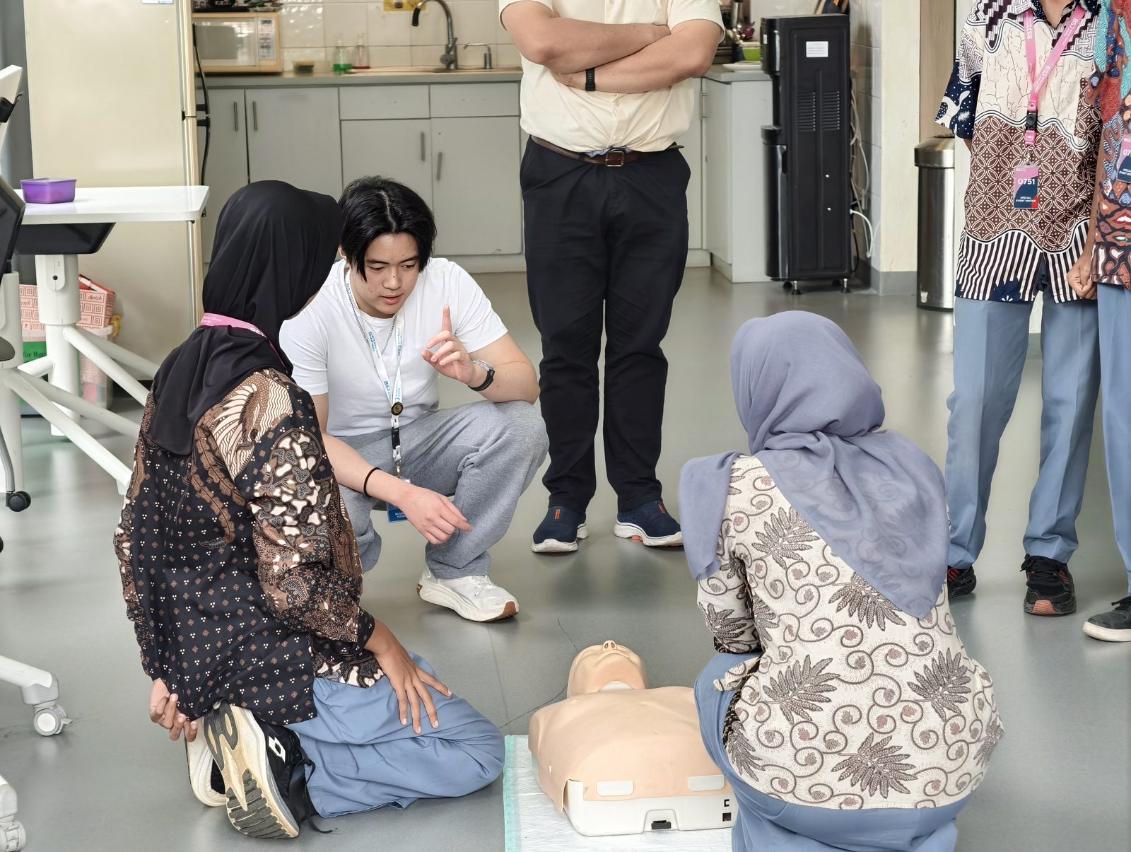 A CPR instructor coaching two students beside a training manikin