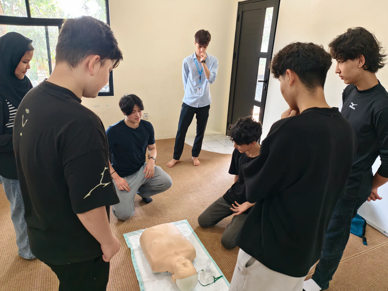 Students gathered around a CPR training manikin during a Beatkeepers workshop