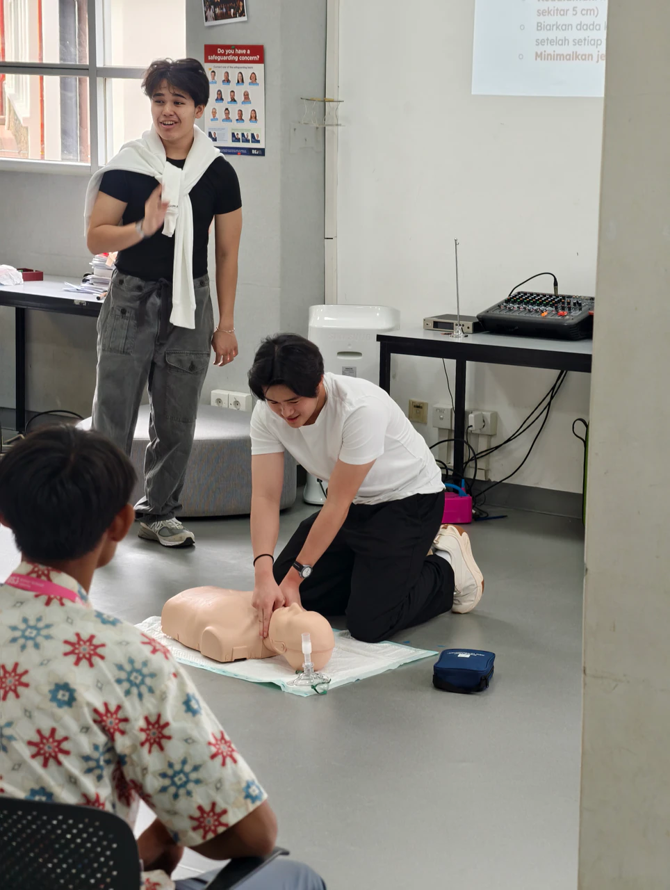 A volunteer demonstrating chest compressions on a training manikin while another volunteer speaks