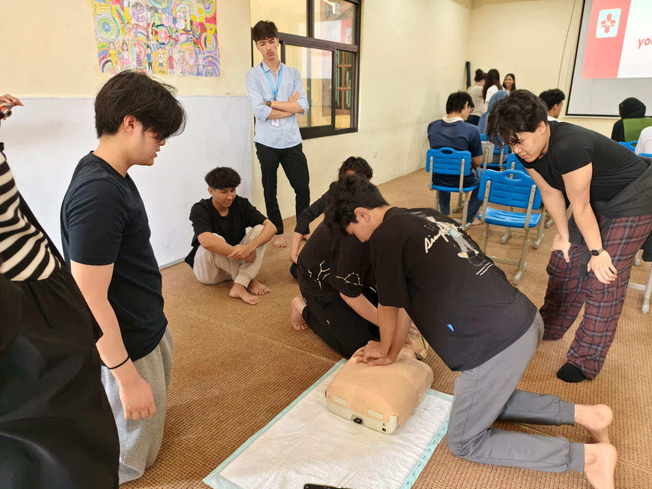 A student practicing chest compressions as other workshop participants watch