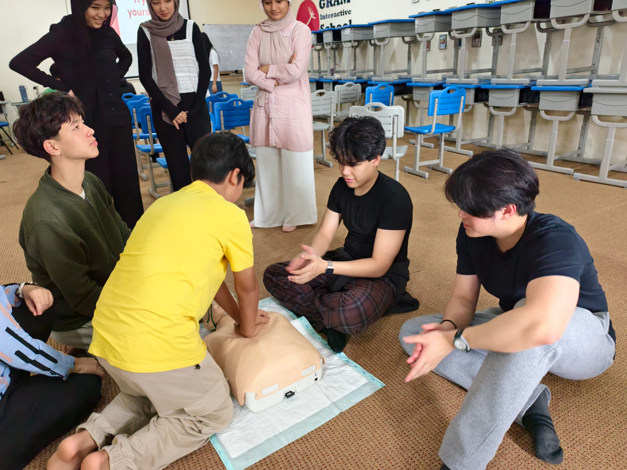 Students and volunteers working together around a CPR training manikin