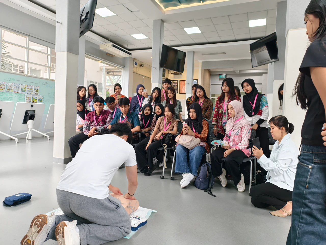 A volunteer demonstrating CPR on a training manikin in front of workshop participants